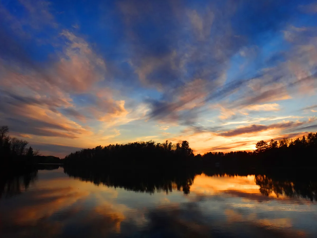Sunset reflected in still Northwoods water beneath a wooded shoreline